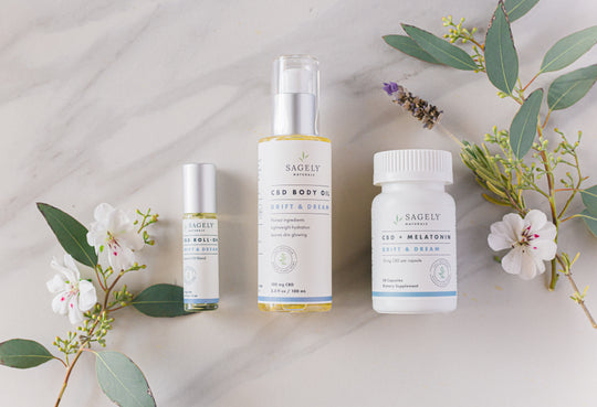 Sagely Naturals Drift & Dream CBD Collection: CBD Body Oil, CBD Roll-On and CBD Capsules next to florals, on top of a granite counter