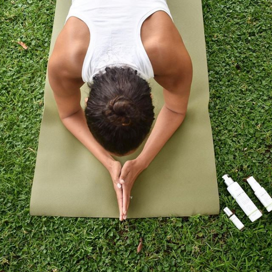 A woman practising yoga in prayer position with Sagely Naturals products on grass.