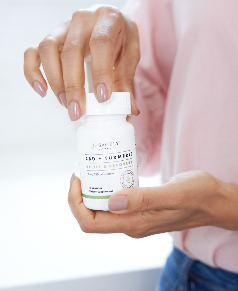 Woman taking cap off of Sagely Naturals Relief & Recovery CBD + Turmeric capsules