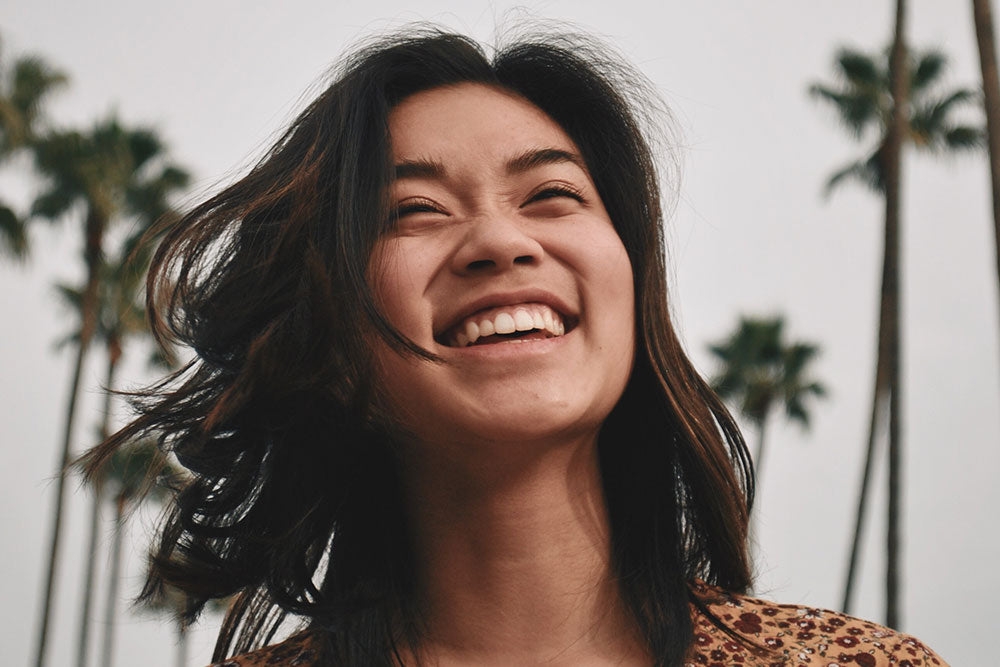 Close up of woman smiling standing in front of a row of palm trees.