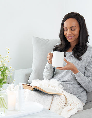 Sagely Naturals Calm & Centered Cream sitting on a table in front of woman drinking out of a white mug and reading a book.