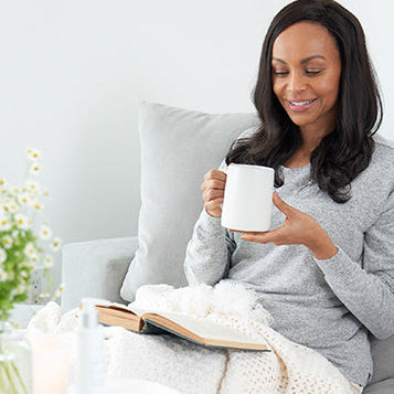 Sagely Naturals Calm & Centered Cream sitting on a table in front of woman drinking out of a white mug and reading a book.