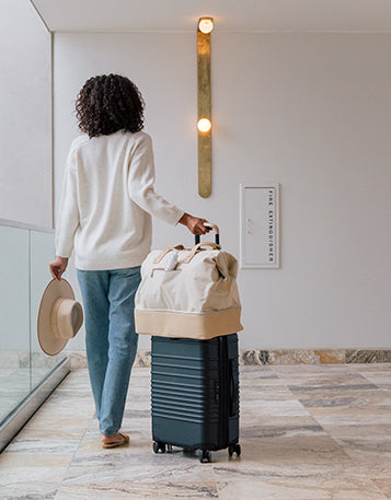 A woman rolling her suitcase and carry o, with Sagely Naturals CBD Cream, through a hotel
