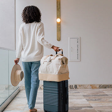 A woman rolling her suitcase and carry o, with Sagely Naturals CBD Cream, through a hotel