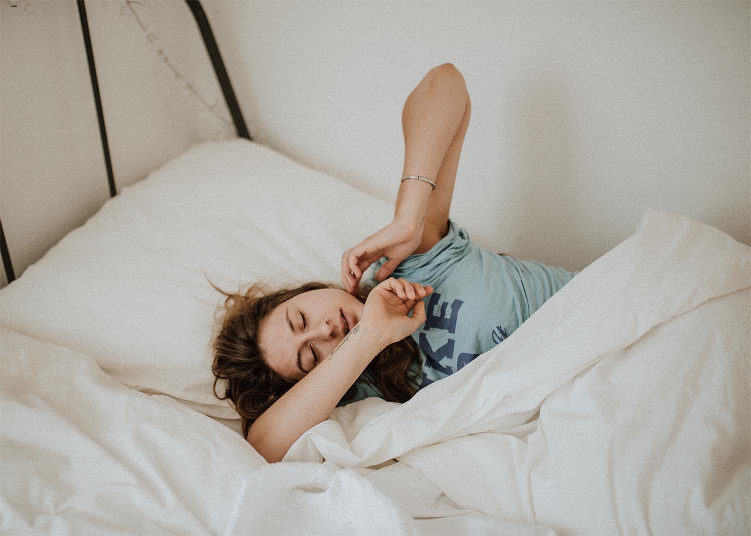A woman waking up and stretching in a bed with white sheets