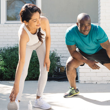 A woman and man in workout clothes stretching outside.