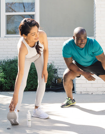 A woman and man in workout clothes stretching outside.