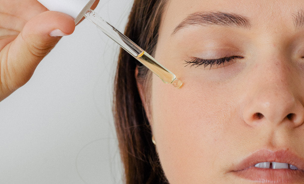 A woman with eyes closed applying oil to her skin.