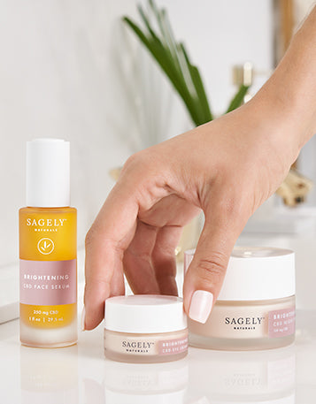 The Sagely Naturals Brightening CBD Skincare collection with a hand grabbing the Sagely Naturals Brightening CBD Eye Cream.