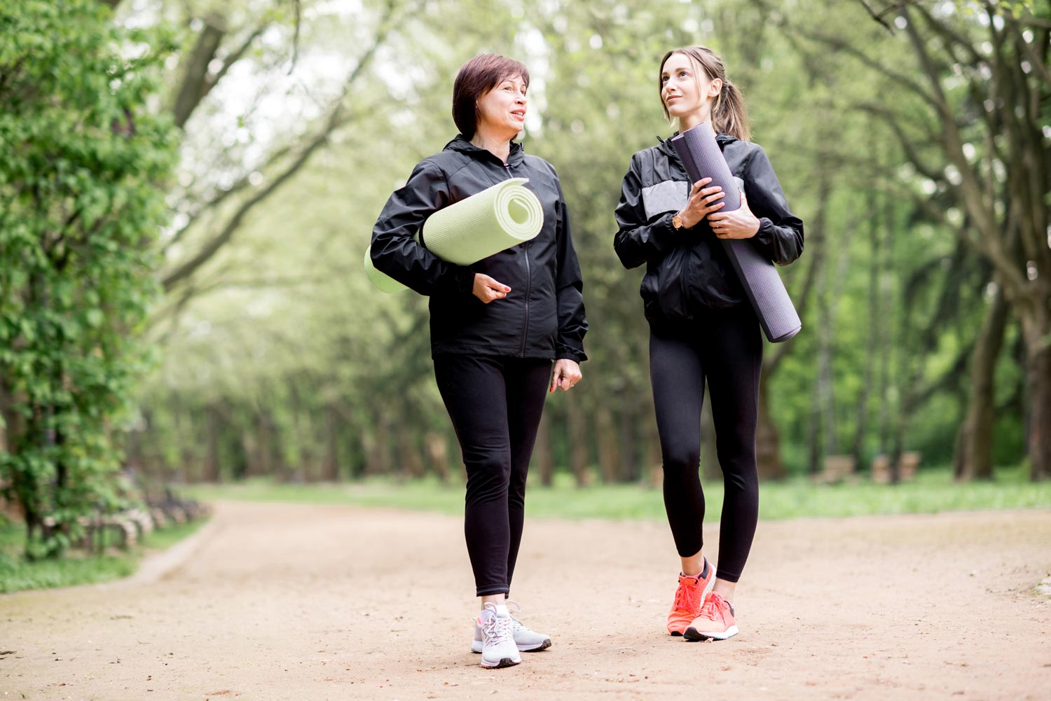 A mom and daughter walking outside holding yoga mats, practicing whole self wellness