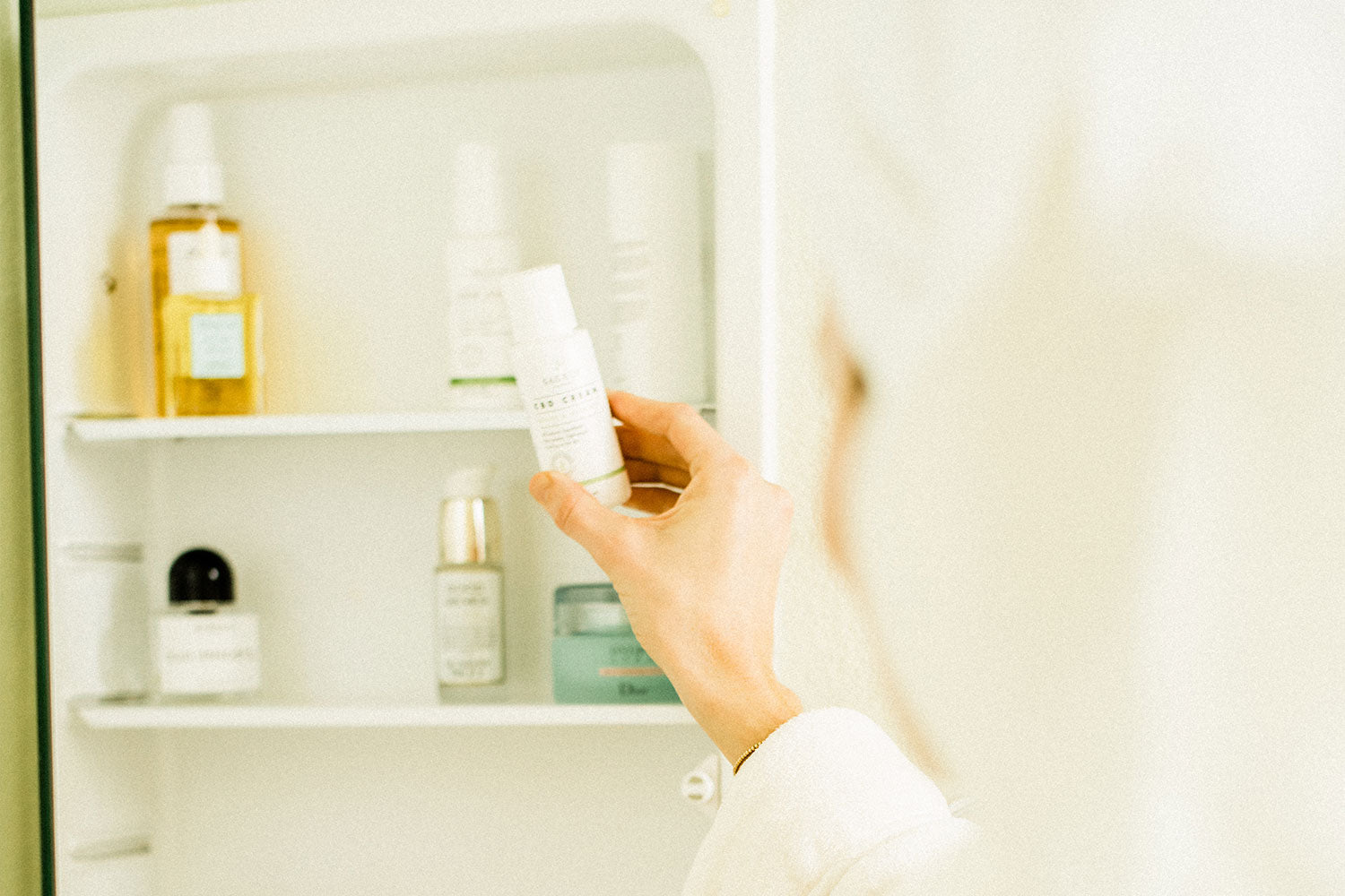 A woman wearing a towel in her hair reaching into her medicine cabinet for Sagely Naturals CBD products
