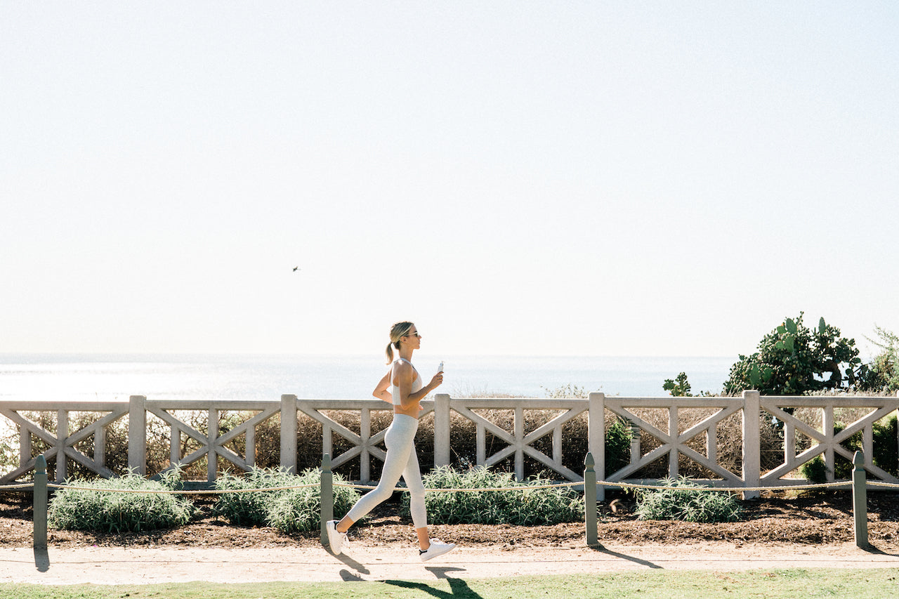 A woman running along an esplanade holding a bottle of Sagely Naturals CBD Cream.