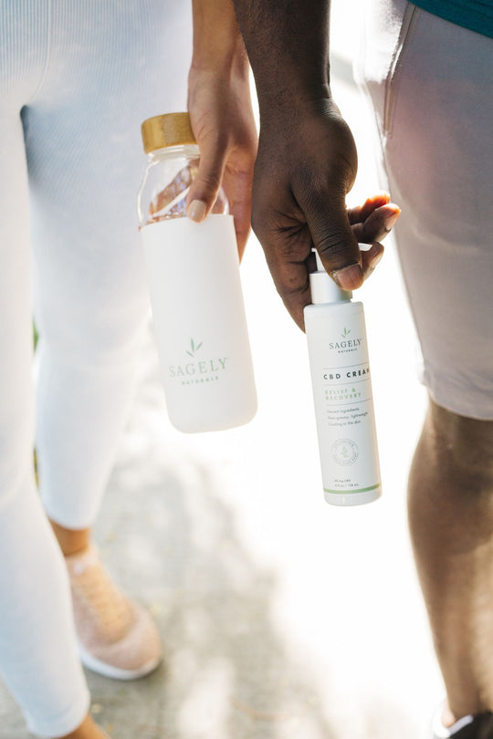 Two people walking carrying a Sagely Naturals water bottle and a Sagely Naturals CBD Cream Relief & Recovery bottle.