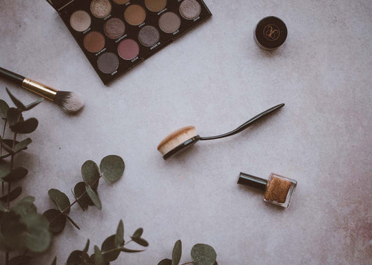 A photo of makeup brushes and makeup lying on a counter top with eucalyptus leaves