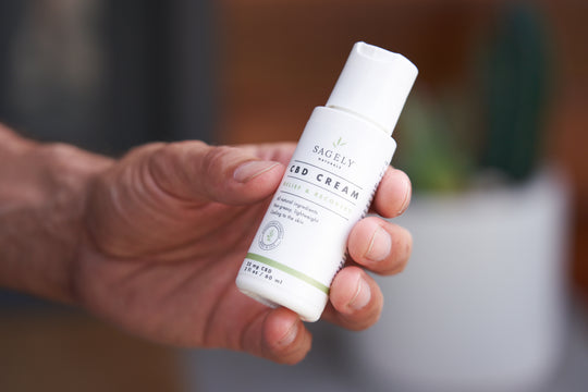 A man holding Sagely Naturals Relief & Recovery CBD Cream; Travel sized