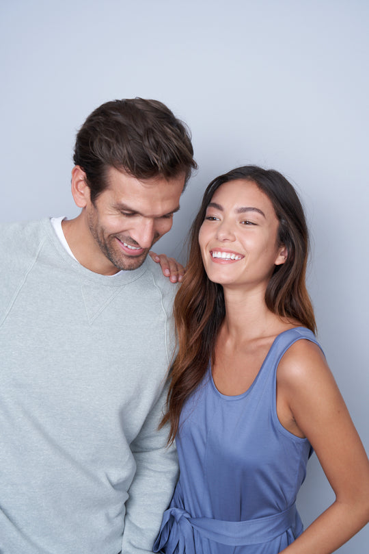 A woman with her hand on a man's shoulder who is leaning in laughing.