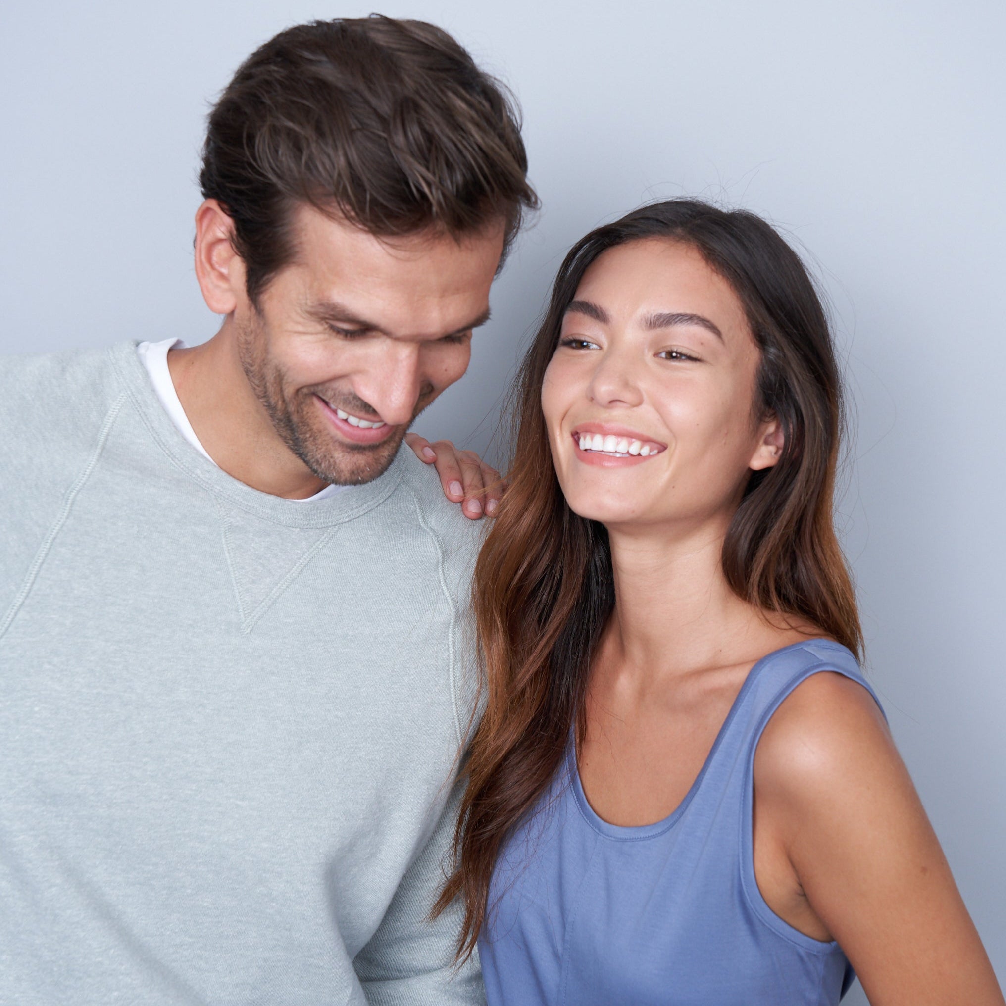 A woman with her hand on a man's shoulder who is leaning in laughing.