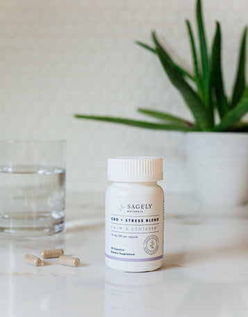 Sagely Naturals Calm & Centered CBD capsules on a bench next to a glass of water and plant.
