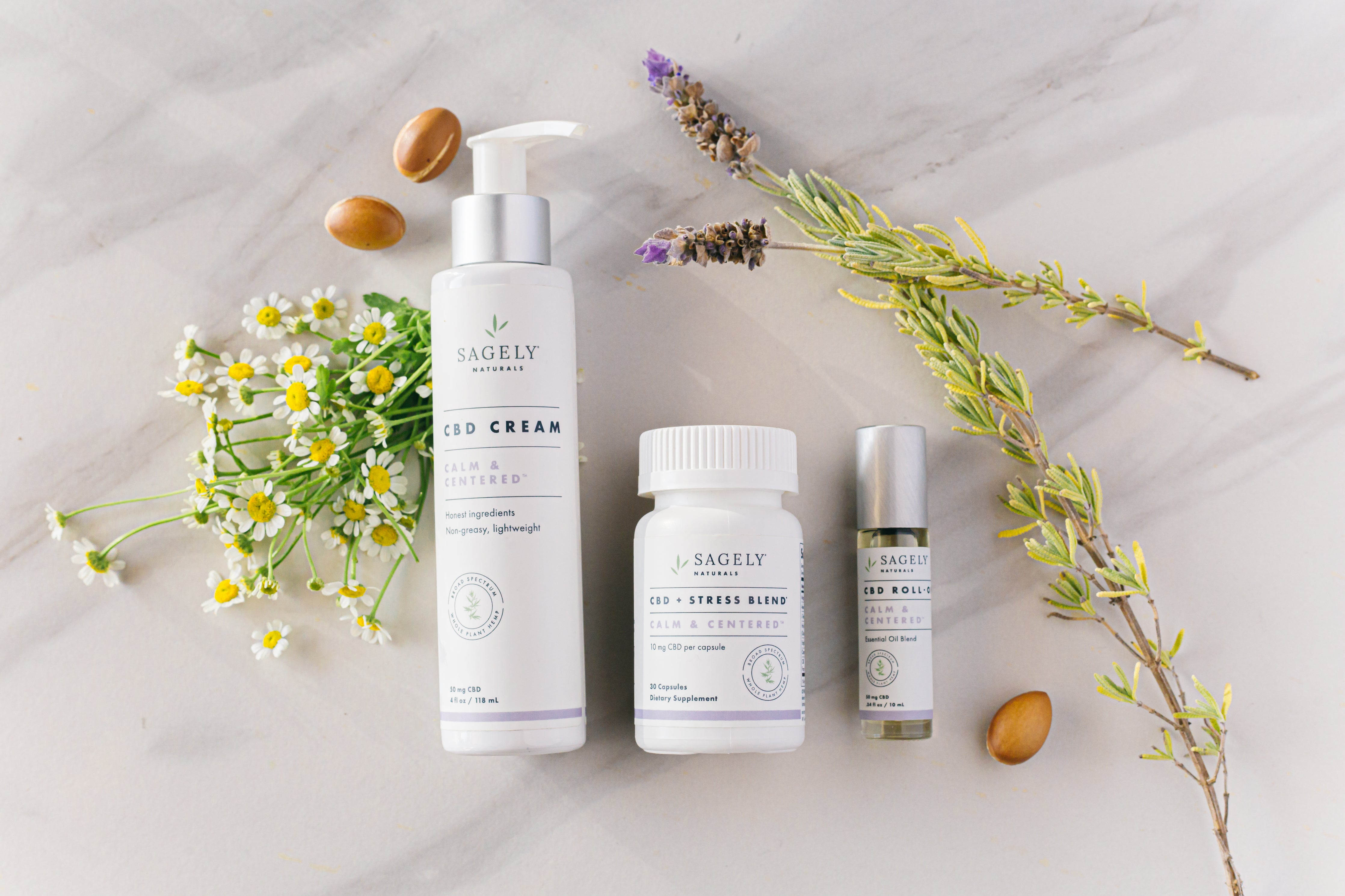 Sagely Naturals Calm & Centered CBD Roll On, CBD Capsules and CBD Cream on a marble table with botanicals