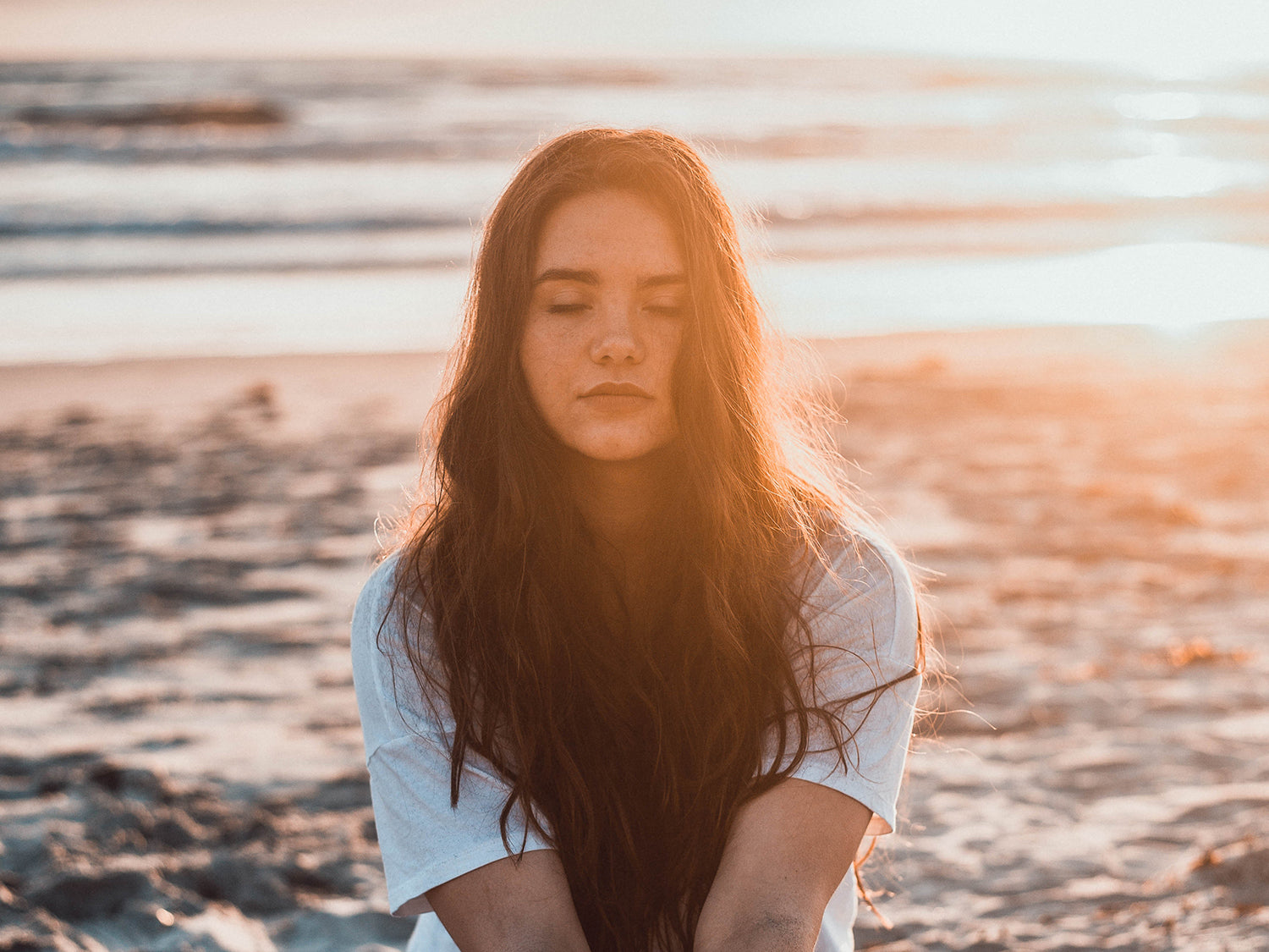 A woman meditating on a beach at sunset