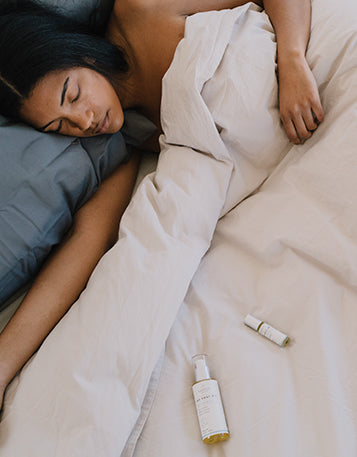 A woman lying under the bed covers sleeping with Sagely Naturals products next to her.