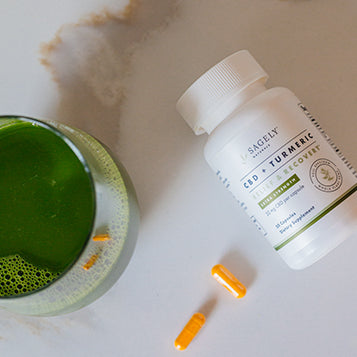 Sagely Naturals Relief & Recover CBD & Turmeric capsules next to a glass of green juice.
