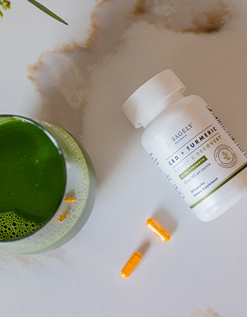 Sagely Naturals Relief & Recover CBD & Turmeric capsules next to a glass of green juice.