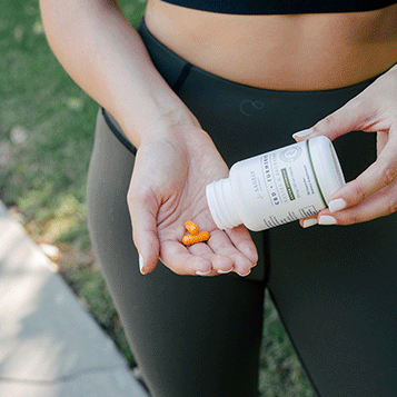 A woman in workout clothes pouring some Sagely Naturals Relief & Recovery CBD Capsules into her hand.