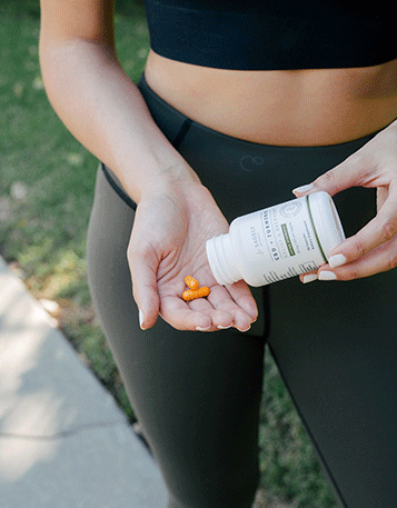 A woman in workout clothes pouring some Sagely Naturals Relief & Recovery CBD Capsules into her hand.