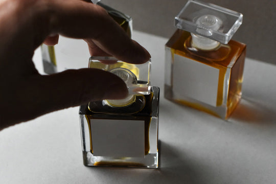 A person’s hand reaching for the lid of a fragrance bottle sitting on a bench.