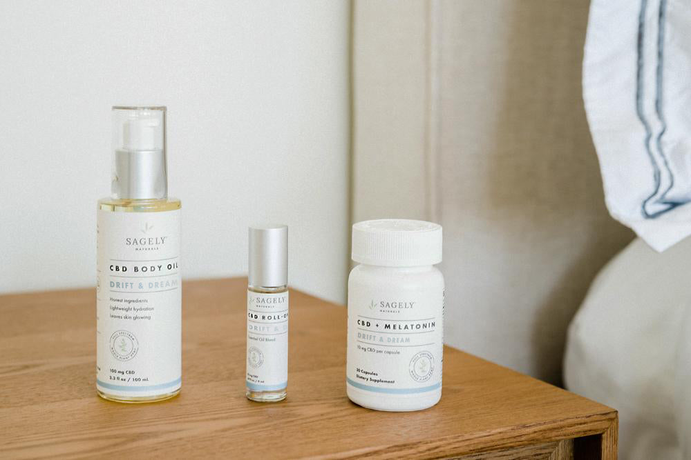 The Sagely Naturals Drift & Dream CBD products sitting on a light wood nightstand by a beautifully styled bed.