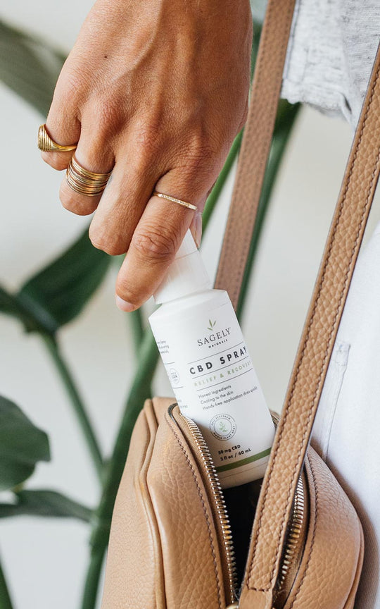A Woman taking out of her purse her Sagely Naturals Relief & Recovery CBD Spray