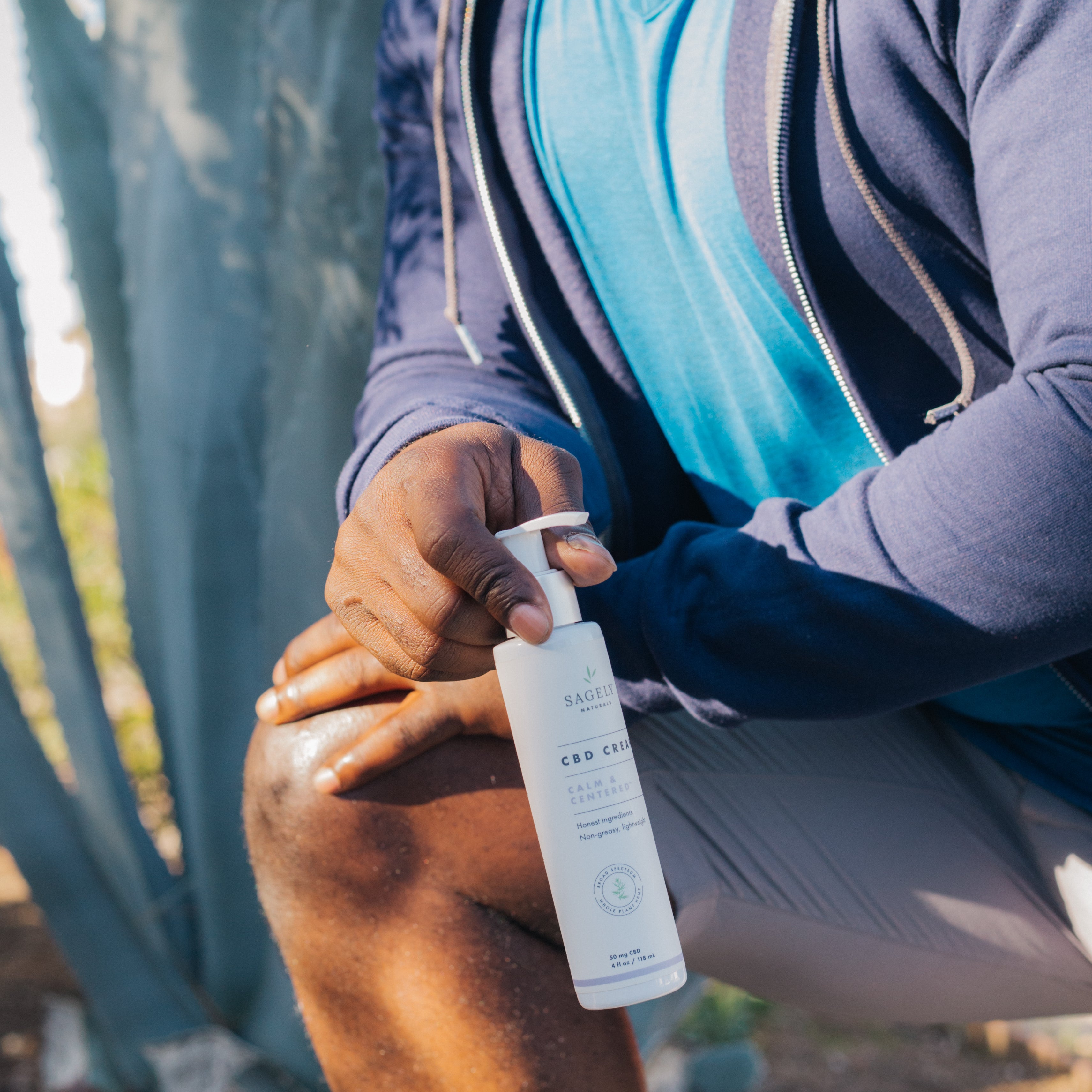 A man in workout clothes leaning into a knee stretch while holding Sagely Naturals Calm & Centered Cream