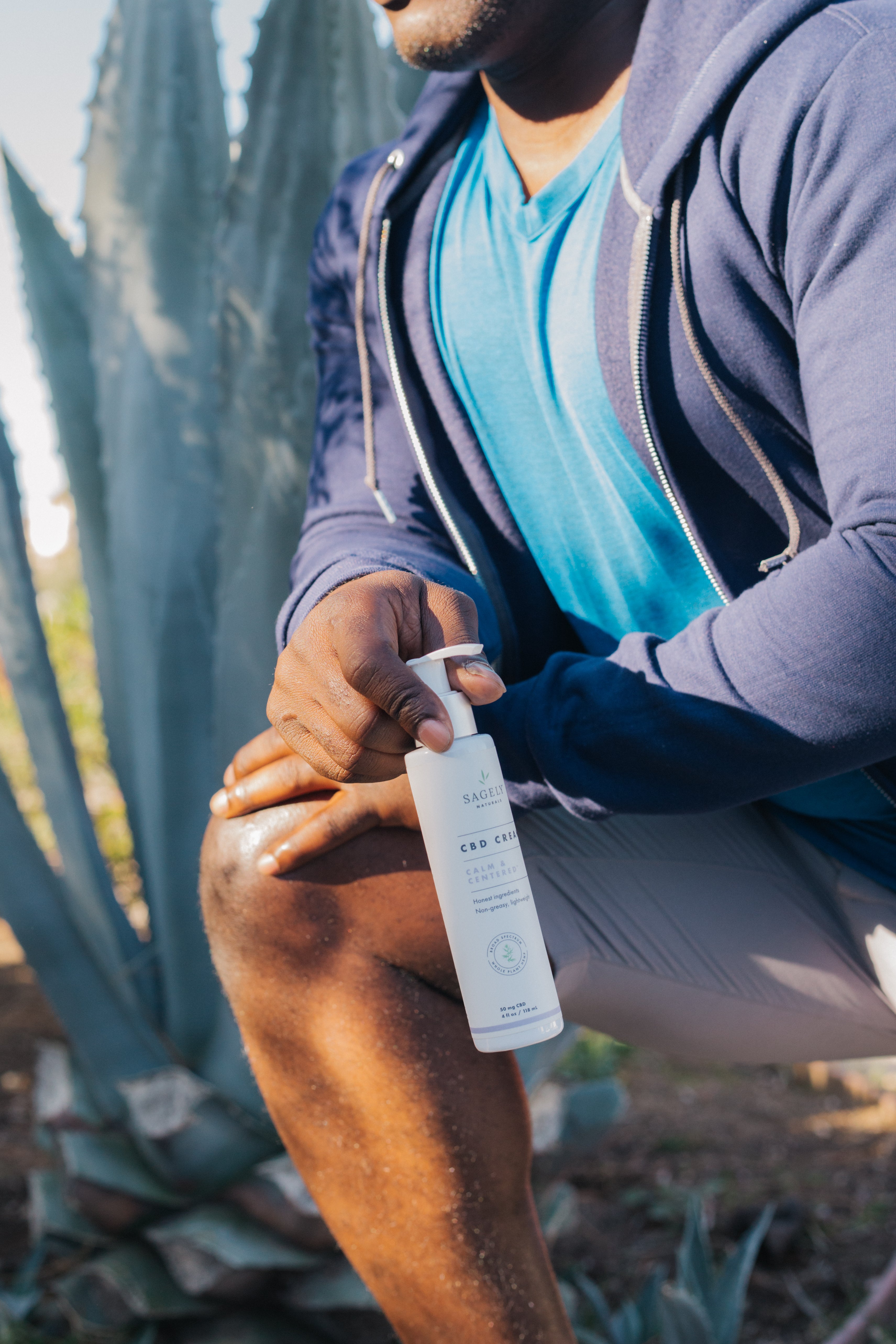 A man in workout clothes leaning into a knee stretch while holding Sagely Naturals Calm & Centered Cream