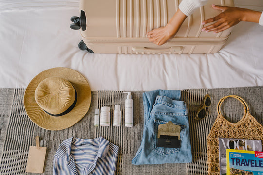 Sagely Naturals CBD products lying on bed next to suitcase, hat, sunglasses.