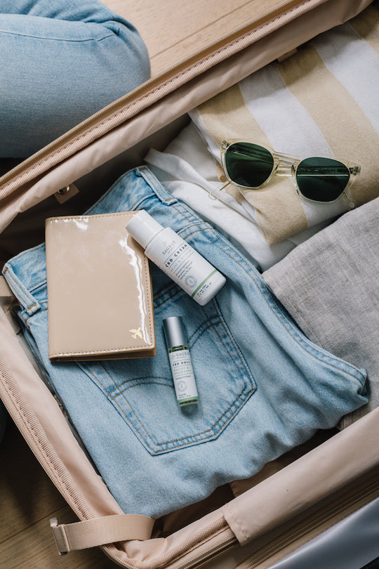 Open suitcase with a diary, sunglasses, clothing, and Sagely Naturals CBD cream and roll-on bottles.